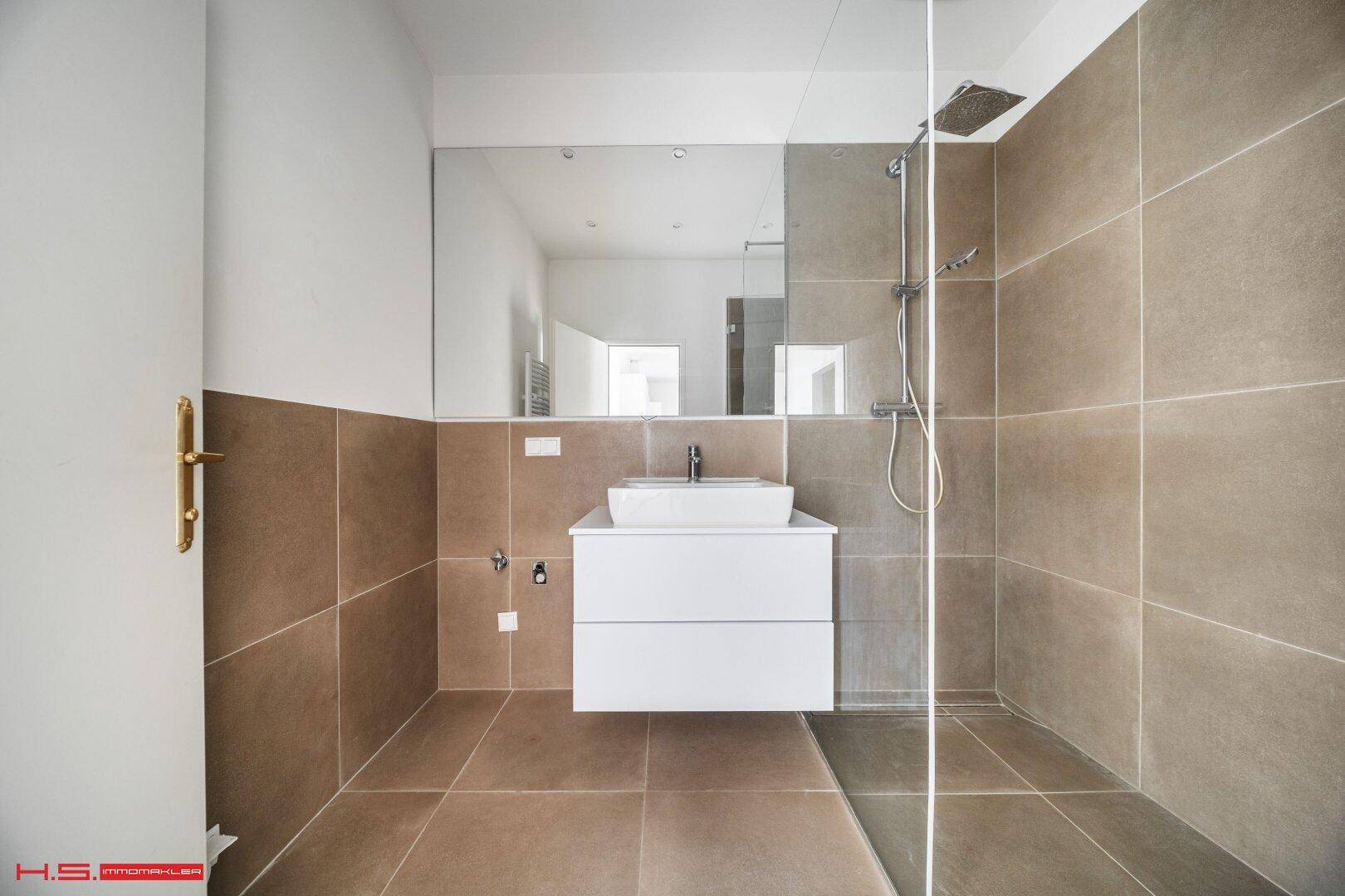 Modernes Badezimmer mit großer Dusche, Waschtisch und großformatigen Fliesen.