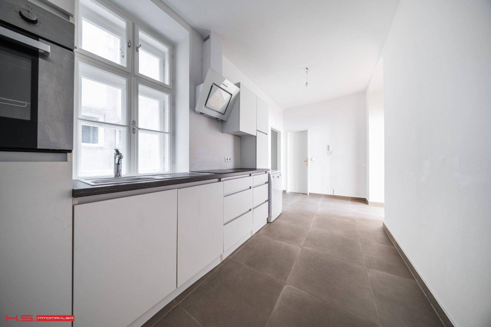 Helle Küche mit weißer Einbauzeile, Spüle unter dem Fenster und Fliesenboden.