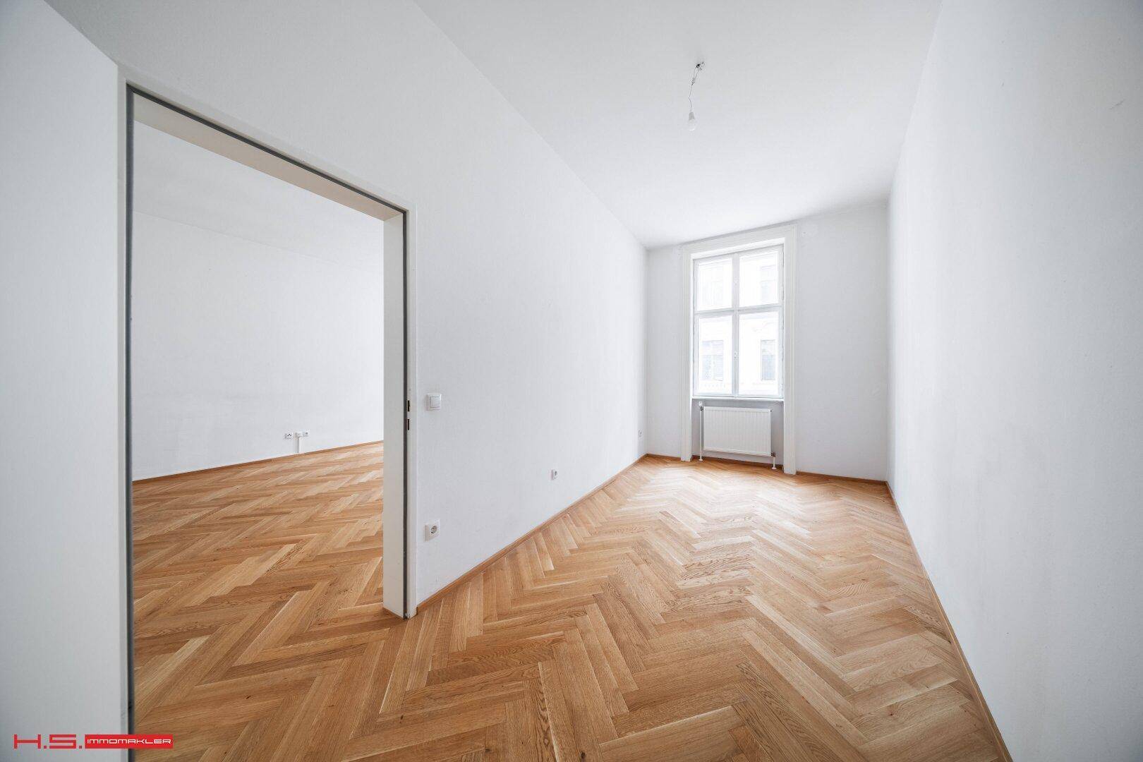 Leeres Zimmer mit Fischgrätparkettboden, weißen Wänden und einem Fenster.