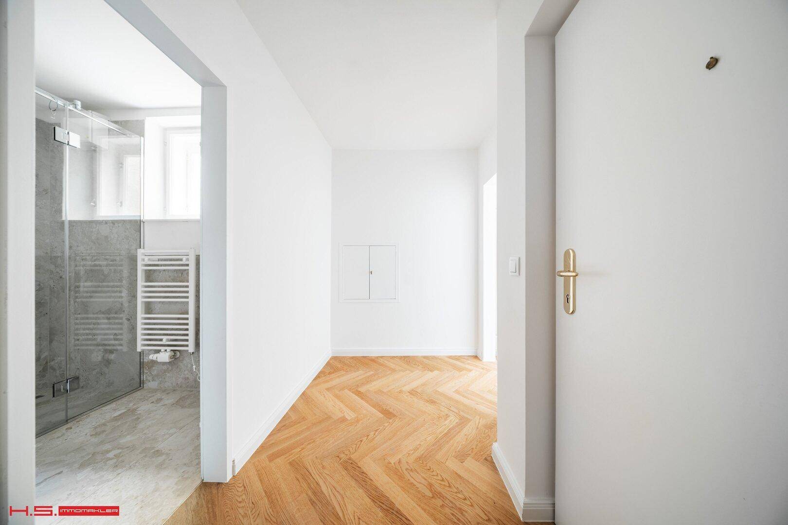 Heller Flur mit Fischgrätparkett, der zu einem modernen Badezimmer führt.