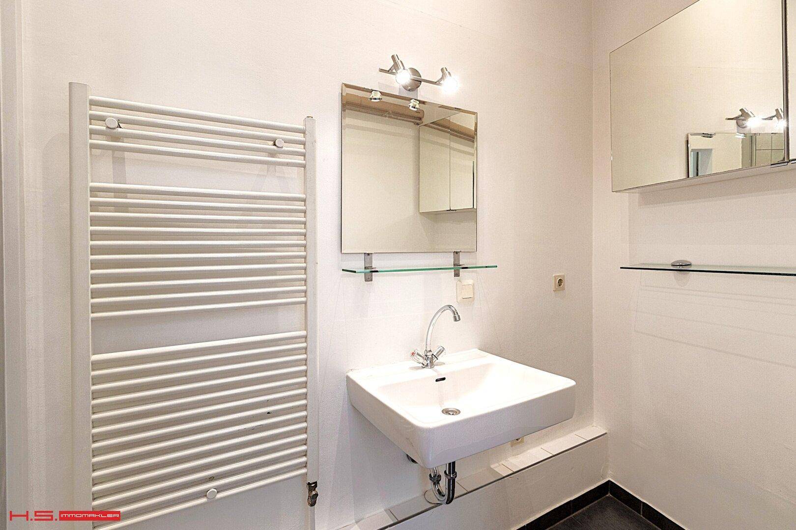 Helles Badezimmer mit Waschbecken, Spiegel und beheiztem Handtuchhalter in schlichtem Design.