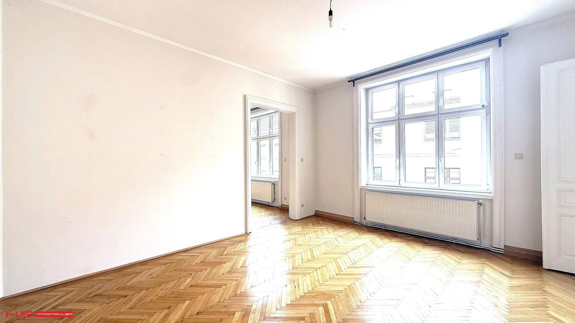 Geräumiges Zimmer mit klassischem Fischgrätparkett und einem großen Fenster, das den Raum erhellt.