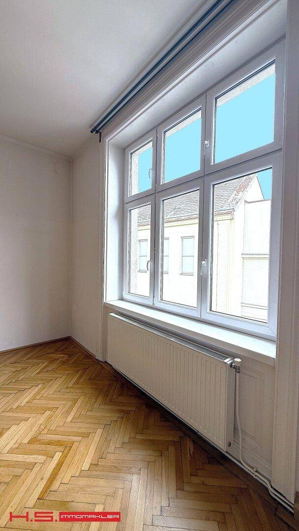 Helles Zimmer mit Fischgrätparkett und einem großen Fenster, das den Blick nach draußen freigibt.