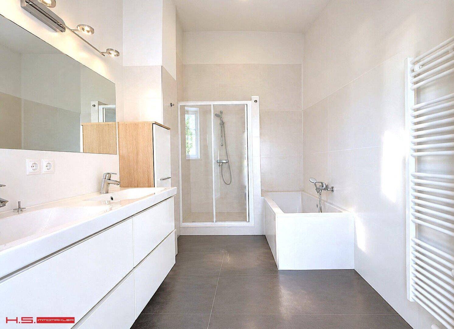 Modernes Badezimmer mit Doppelwaschbecken, Badewanne, Duschkabine und beheiztem Handtuchhalter.