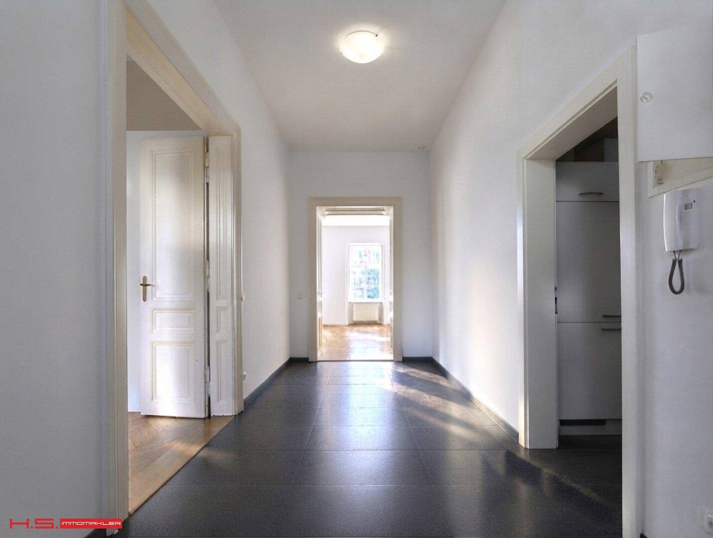 Langer Flur mit dunklen Fliesen und Zugang zu mehreren Zimmern der Wohnung, hell beleuchtet.
