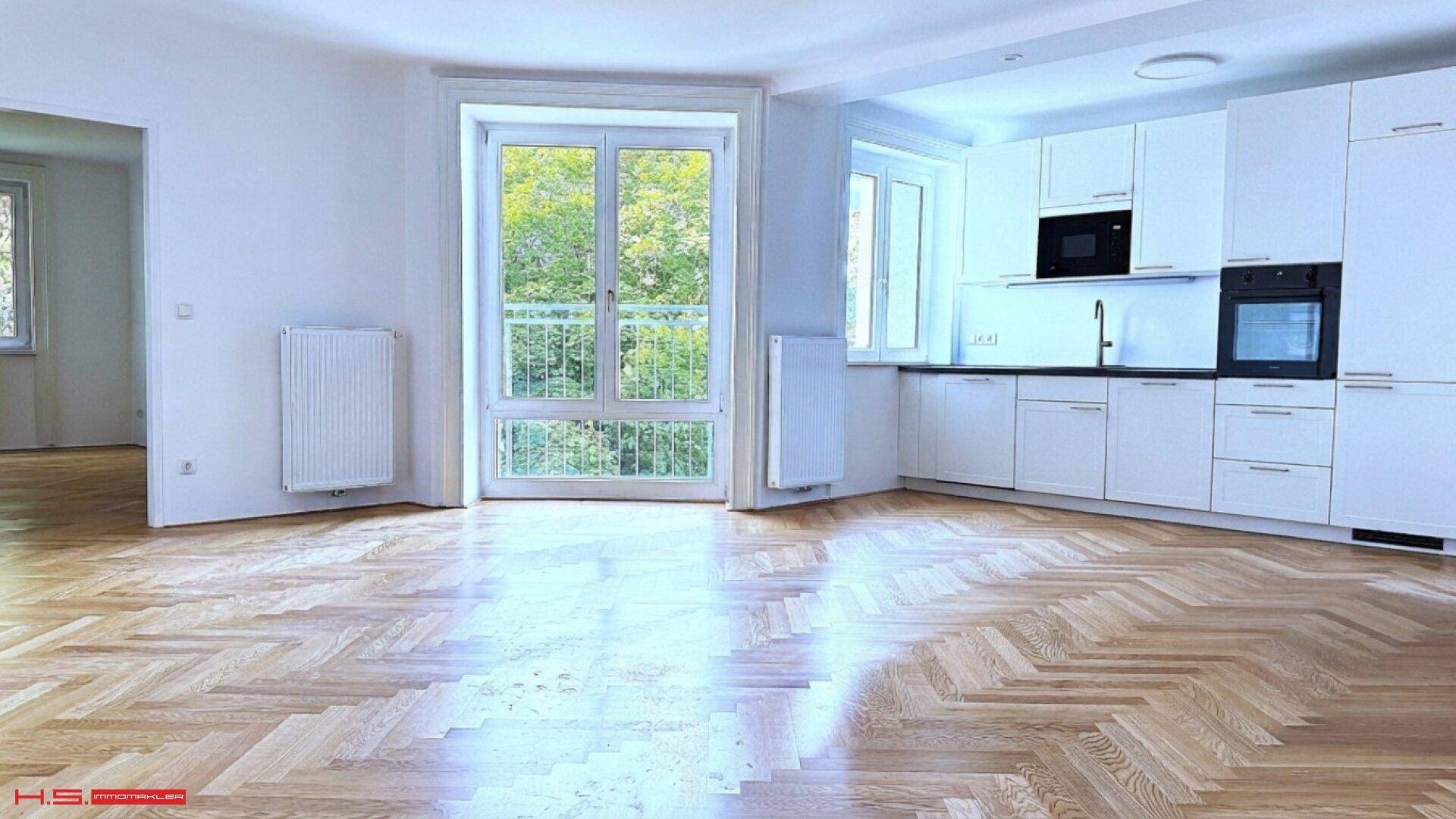 Offene Küche mit weißen Schränken, integrierten Geräten und Blick ins Grüne durch große Fenster.
