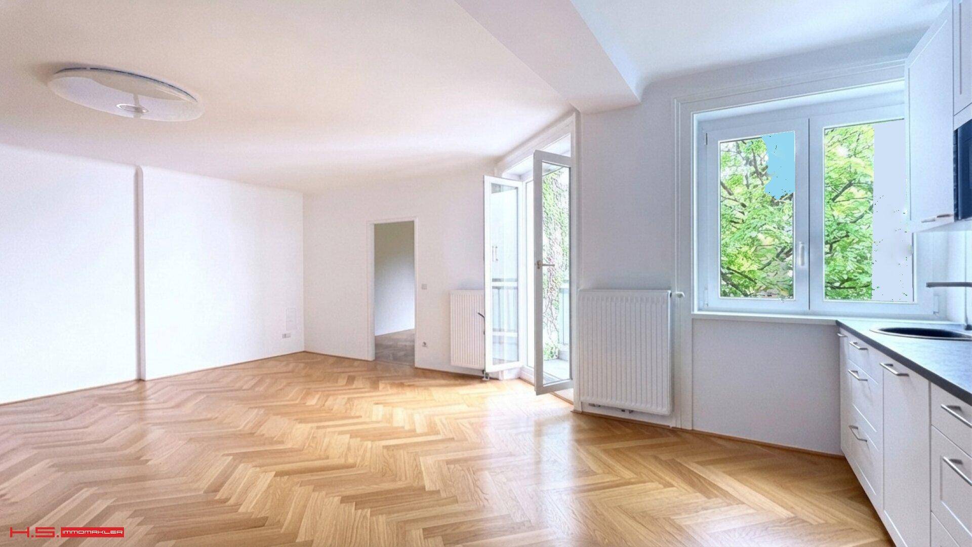 Geräumiger Wohnbereich mit hellem Fischgrätparkett, weißen Wänden und einem französischen Balkon.
