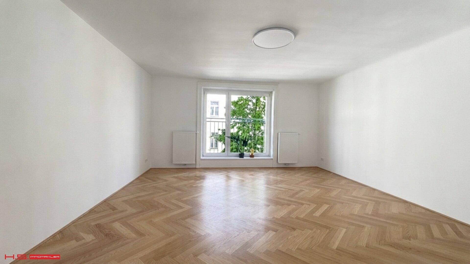 Helles Schlafzimmer mit Fischgrätparkett, weißen Wänden und Blick ins Grüne.