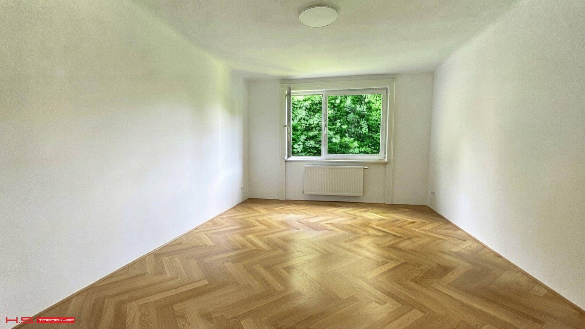 Ruhiges Schlafzimmer mit Fischgrätparkett und Fenster mit Blick auf üppiges Grün.