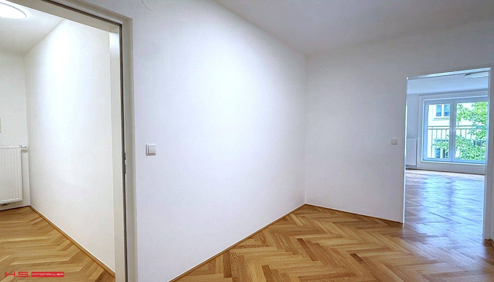 Heller Flur mit Fischgrätparkett und weißen Wänden, der zu weiteren Räumen führt.