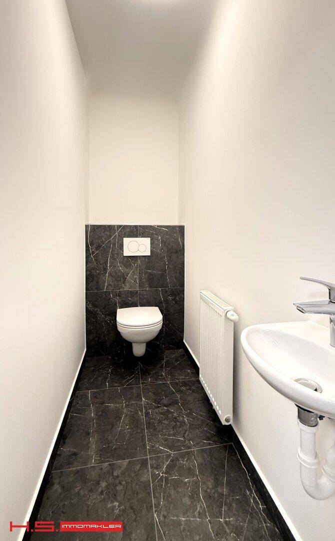 Modernes Gäste-WC mit Wand-WC, kleinem Waschbecken und dunklen Marmorfliesen.