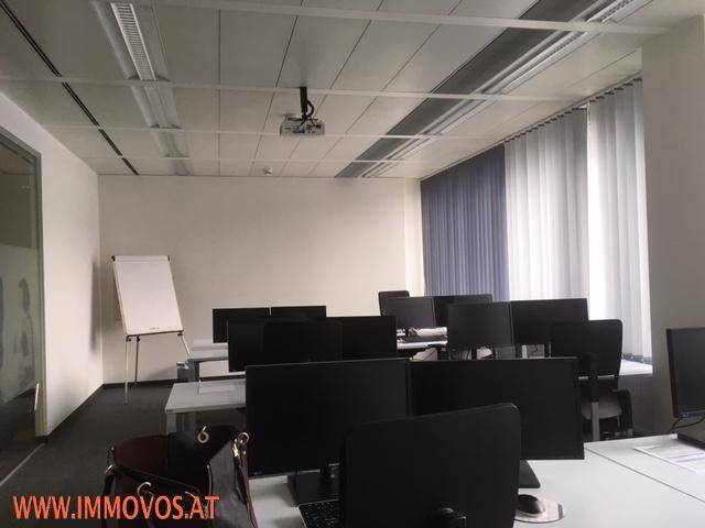 Schulungsraum mit mehreren Computermonitoren, Whiteboard und Jalousien an den Fenstern.