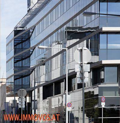 Nahaufnahme einer modernen Glasfassade mit reflektierenden Fenstern und Straßenlaternen.