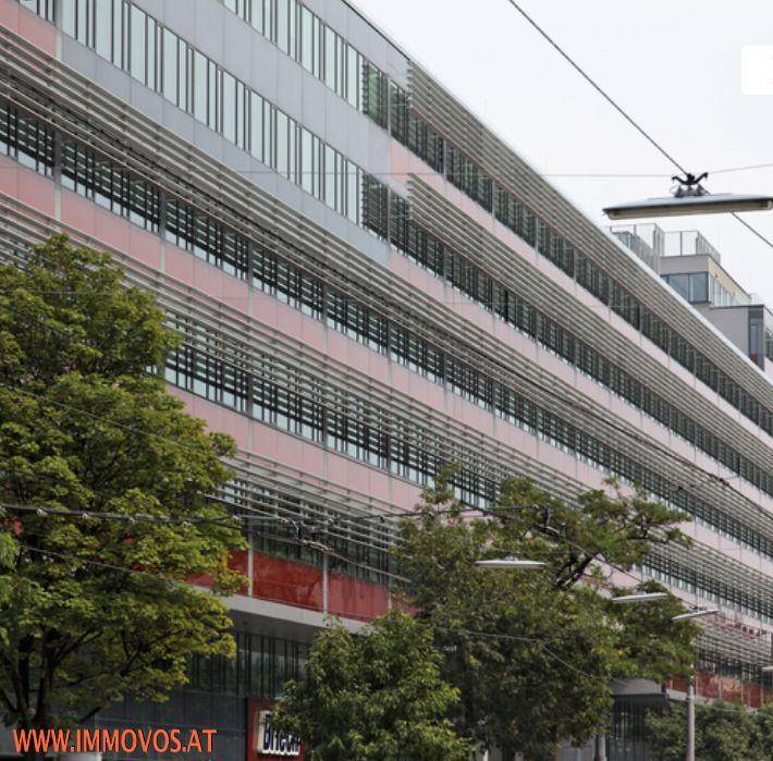 Detailansicht der modernen Gebäudefassade mit horizontalen roten Bändern und vielen Fenstern.