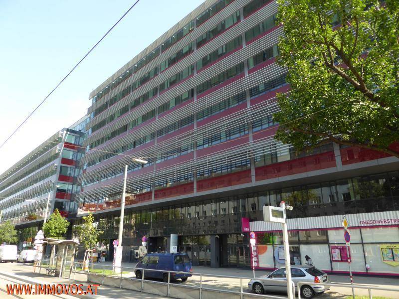 Moderne Bürogebäude-Fassade mit roten Akzenten und großen Fensterfronten an einer belebten Straße.