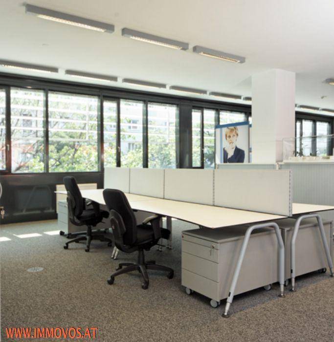 Helle Büroräume mit Reihen von Schreibtischen, ergonomischen Stühlen und viel Tageslicht durch große Fenster.
