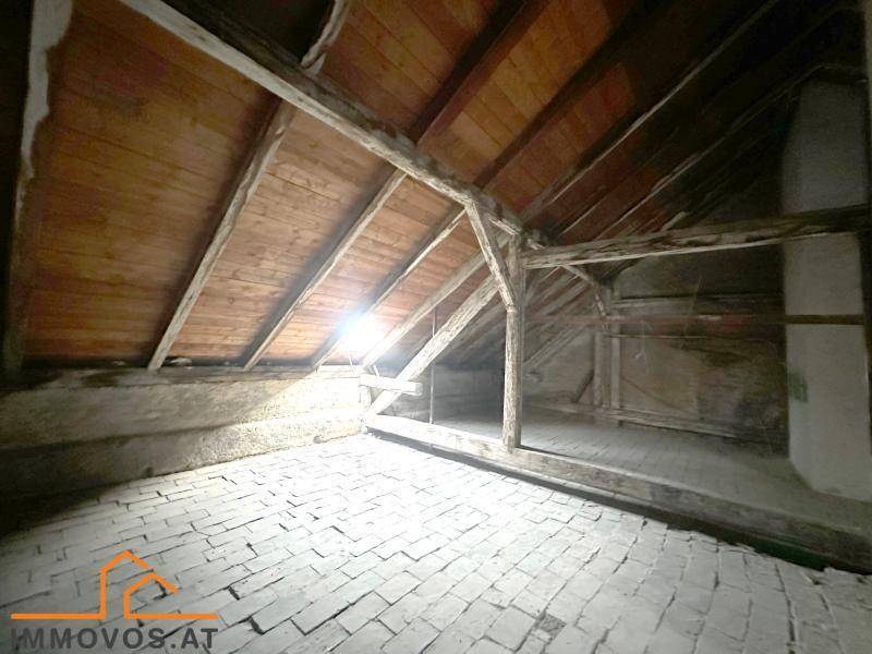 Unausgebauter Dachboden mit sichtbaren Holzbalken und Ziegelboden, bereit für den Ausbau.