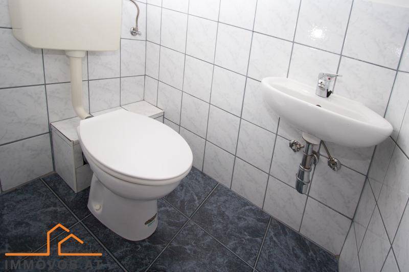 Separates WC mit Toilette, kleinem Waschbecken und weißen Wandfliesen.