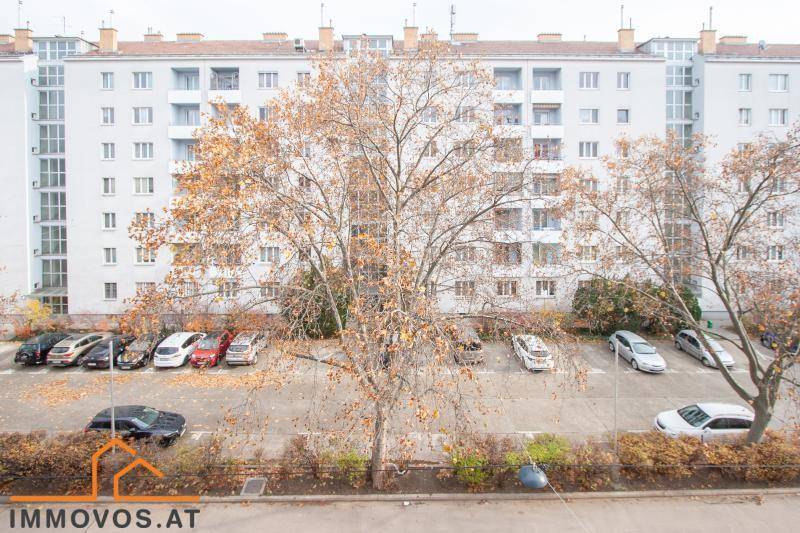 Außenansicht eines Wohngebäudes mit Parkplatz und Bäumen im Vordergrund.