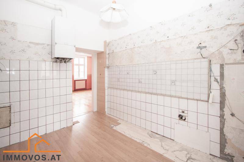 Renovierungsbedürftige Küche mit gefliesten Wänden und Blick in ein angrenzendes Zimmer.