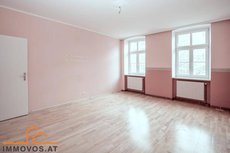 Geräumiges Zimmer mit rosa Wänden, hellem Parkettboden und zwei großen Fenstern.