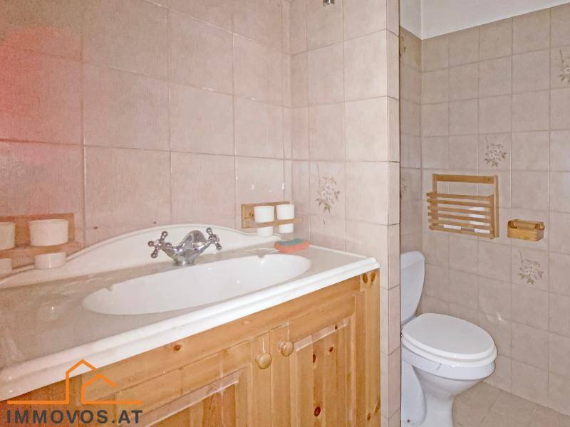 Badezimmer mit WC, Holzwaschtisch und beigefarbenen Wandfliesen.