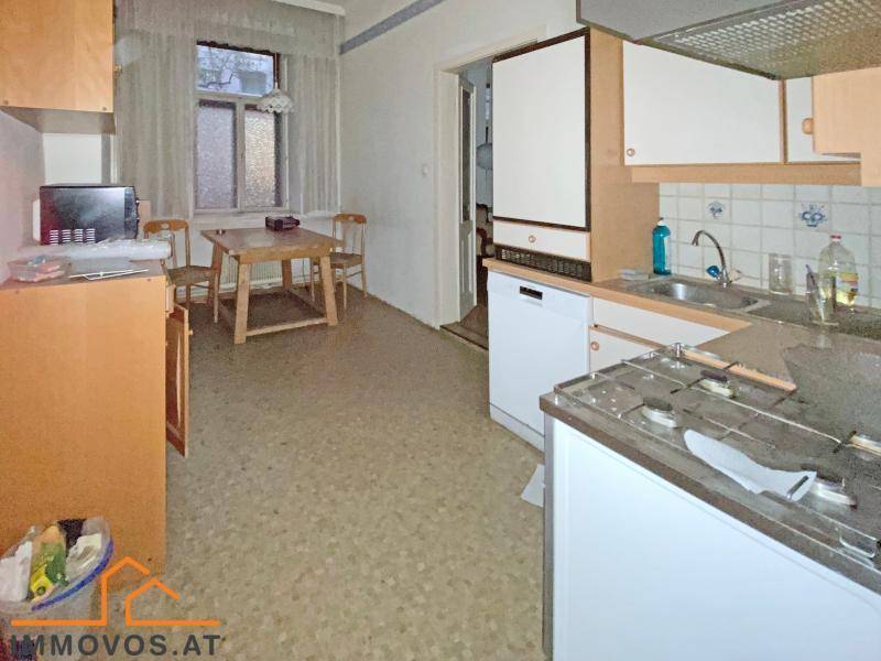 Einfache Küche mit Spüle, Gasherd und kleinem Essbereich am Fenster.