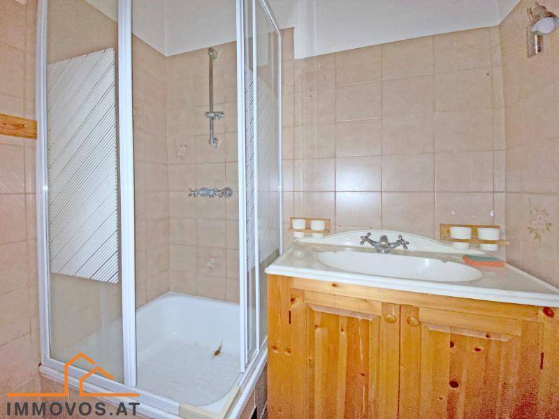 Badezimmer mit Duschkabine, Holzwaschtisch und beigefarbenen Fliesen.