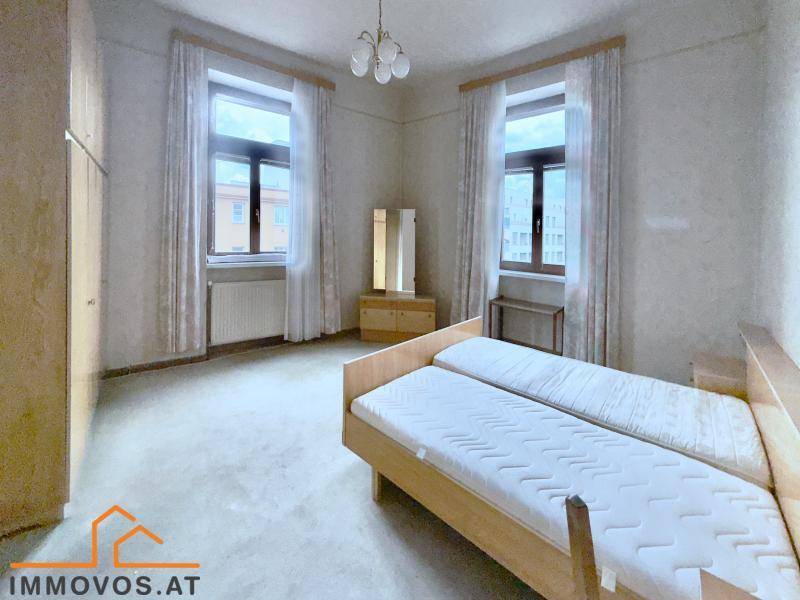 Schlafzimmer mit zwei Einzelbetten, Parkettboden und zwei großen Fenstern.