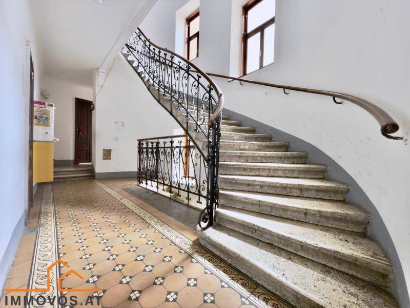 Elegantes Treppenhaus mit schmiedeeisernem Geländer und historischen Fliesen.