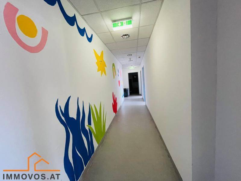 Langer Flur mit weißen Wänden, einer farbenfroh bemalten Wand und abgehängter Decke.