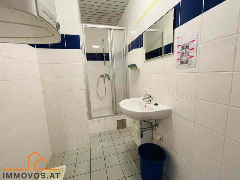 Badezimmer mit weißen Fliesen, blauen Akzenten, einer Duschkabine und einem Waschbecken.