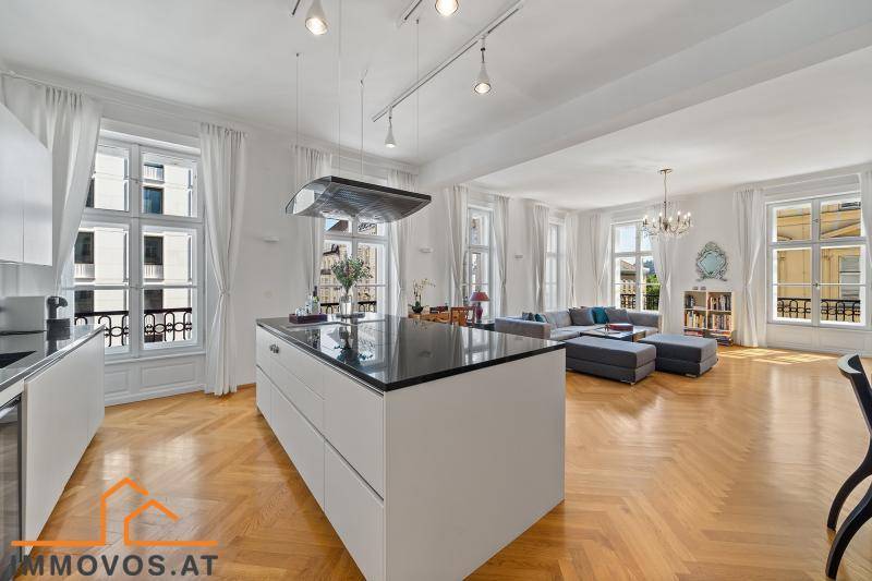 Heller Wohnbereich mit offener Küche, Fischgrätparkett und Blick auf die Stadt durch hohe Fenster.