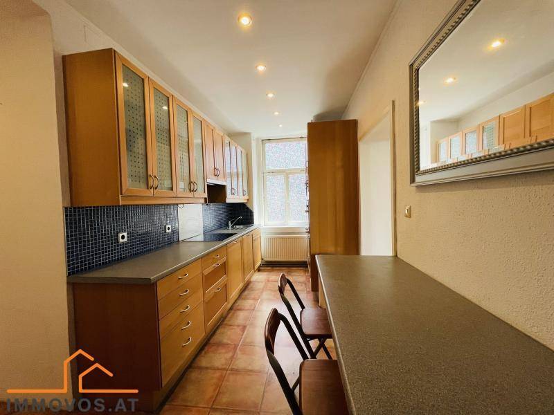 Längliche Küche mit Holzfronten, blauen Fliesen und integriertem Essbereich.