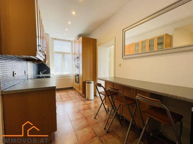 Funktionale Küche mit Holzschränken, dunkler Arbeitsplatte und Essbereich mit Barhockern.