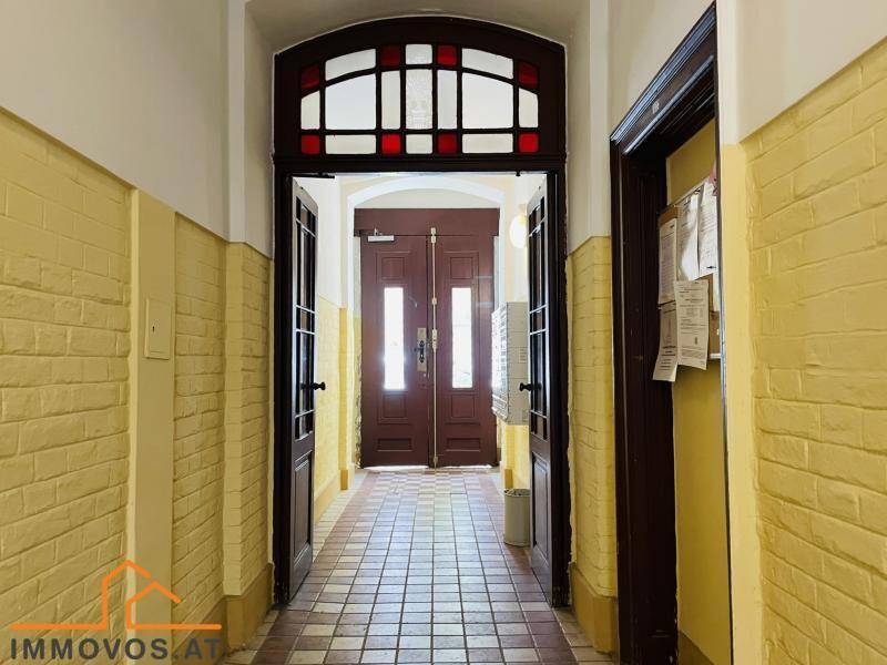 Eingangsbereich eines Altbaus mit doppelten Holztüren und gemustertem Fliesenboden.