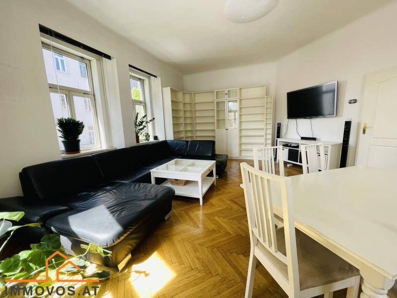 Geräumiger Wohn-Essbereich mit dunklem Sofa, Esstisch und integrierten Bücherregalen.