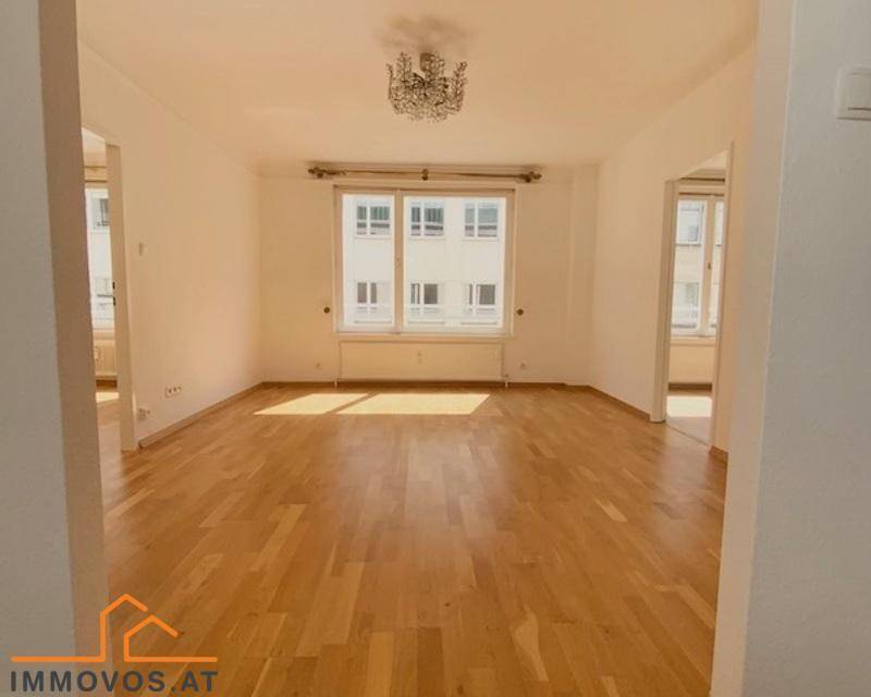 Geräumiges, leeres Wohnzimmer mit hellem Parkettboden und großen Fenstern, die viel Tageslicht hereinlassen.