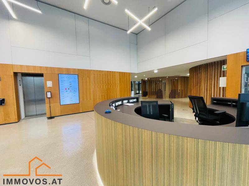 Moderner Empfangsbereich mit geschwungenem Tresen, Aufzug und digitalen Informationsbildschirmen.