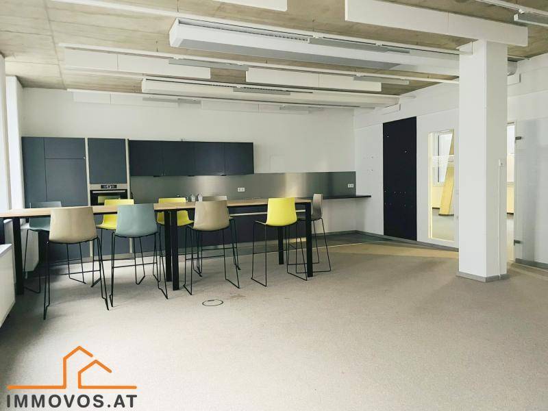 Moderne Büroküche mit dunklen Schränken, langer Theke und bunten Barhockern für Pausen.