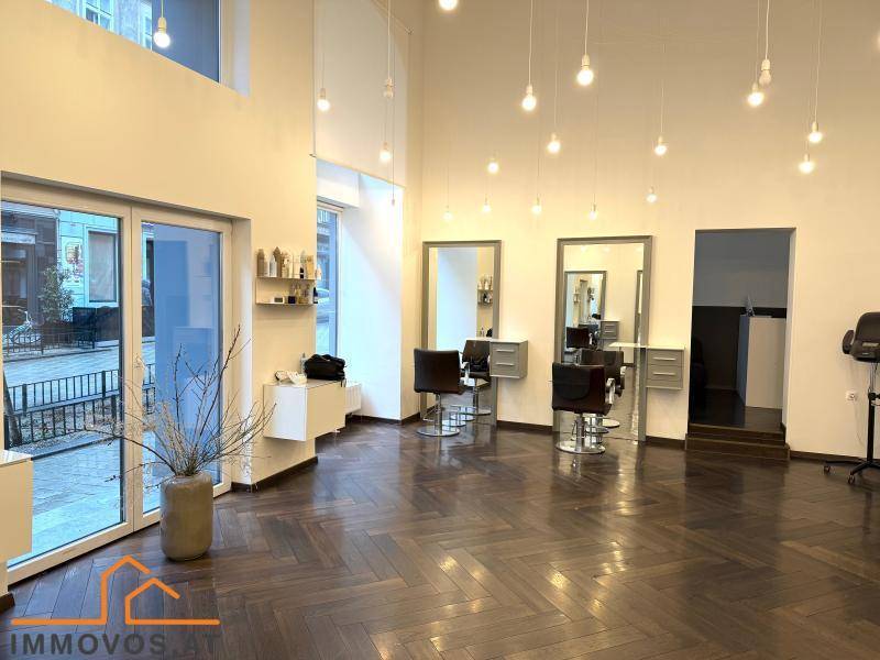 Moderner Friseursalon mit dunklem Fischgrätparkett, hohen Decken und viel Tageslicht durch große Fenster.