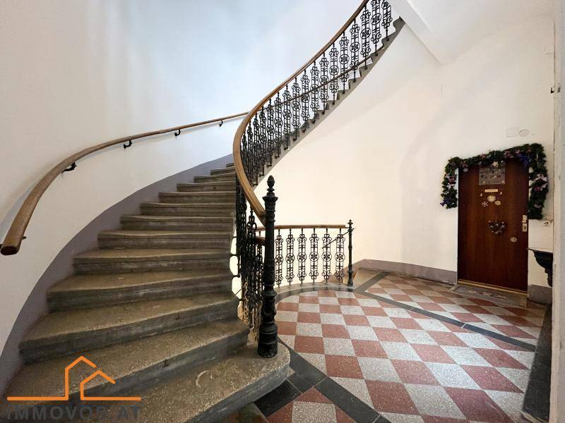 Elegantes Treppenhaus mit geschwungener Steintreppe, schmiedeeisernem Geländer und gemustertem Boden.