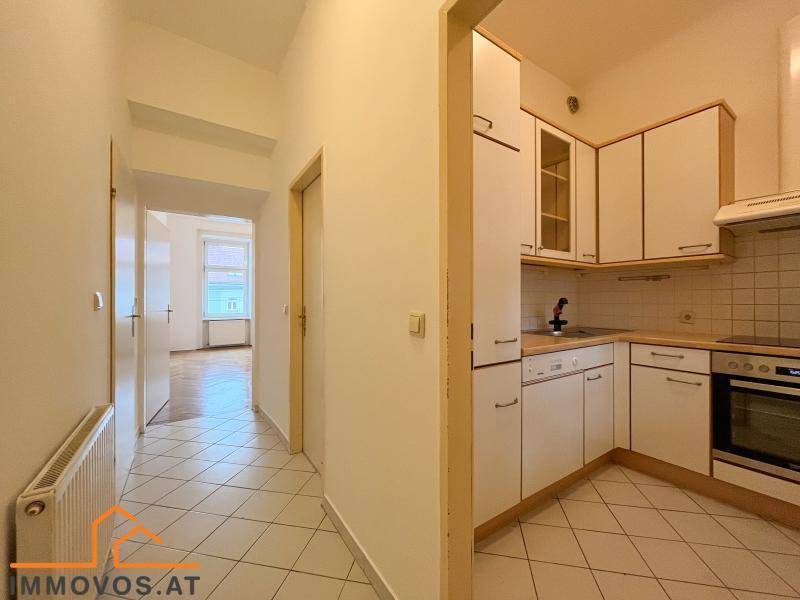 Heller Flur mit Fliesenboden, der zu einer funktionalen Küche mit weißen Schränken führt.