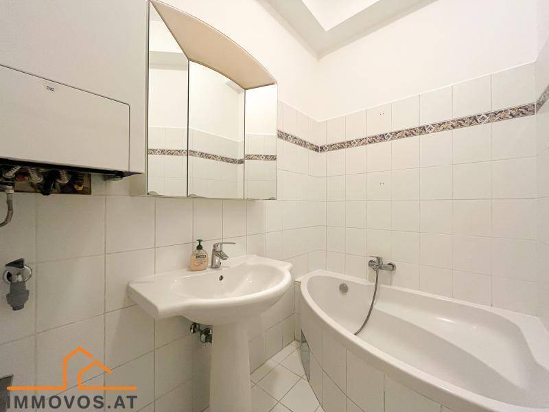 Badezimmer mit weißer Badewanne, Waschbecken und hellen Fliesen, inklusive Spiegelschrank.