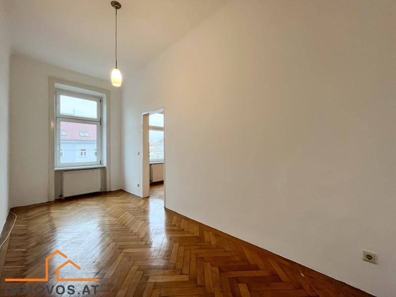 Leeres Zimmer mit glänzendem Fischgrätparkett und einem großen Fenster, das viel Licht hereinlässt.