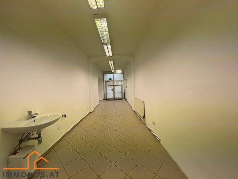 Gefliester Flur mit Waschbecken an der Wand, Heizkörper und Deckenleuchten, ideal für Gewerbe.