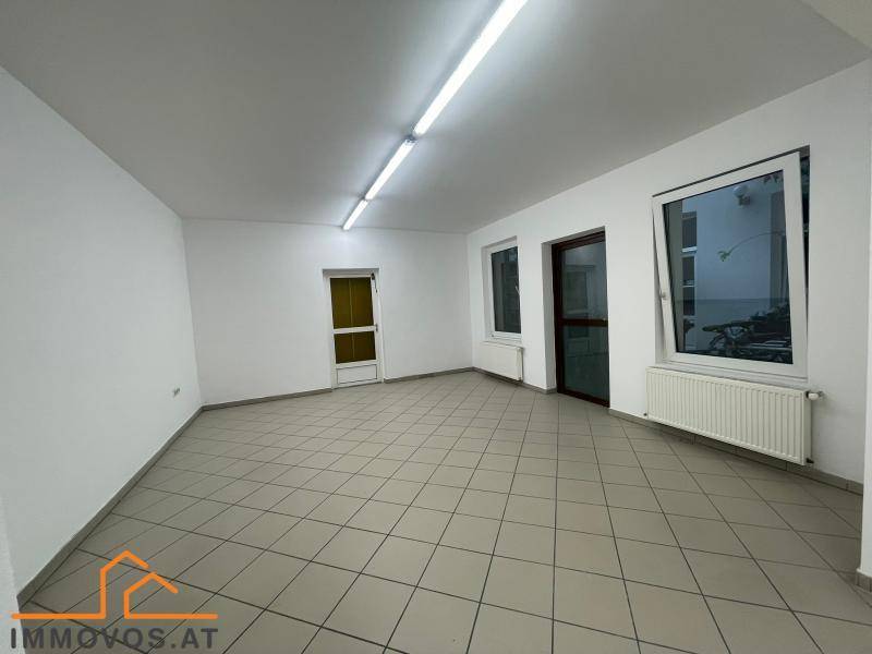 Heller Gewerberaum mit Fliesenboden, Heizkörpern unter den Fenstern und einer langen Deckenleuchte.