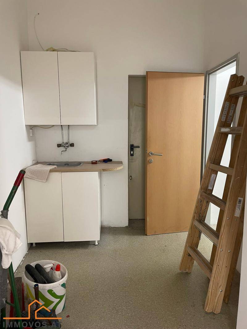 Kleine Küchenzeile mit weißen Schränken, Spülbecken und einer Leiter im Raum.
