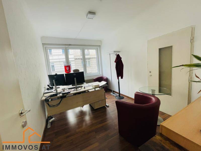 Einzelbüro mit großem Fenster, Schreibtisch und zwei roten Sesseln für Besucher.