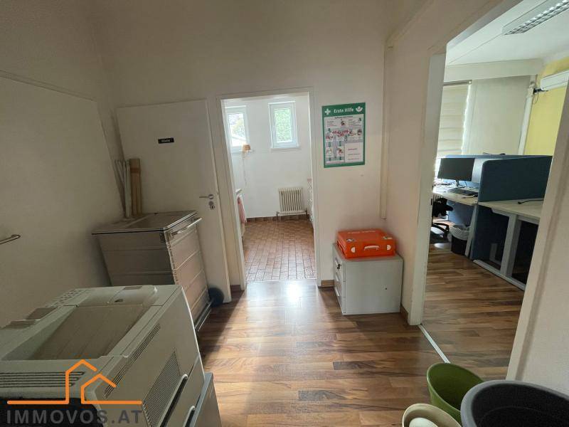 Flur mit Drucker und Zugang zu einem weiteren Raum, möglicherweise einer Teeküche oder einem Bad.